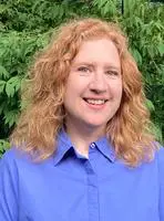 A woman with red hair and blue shirt smiling.